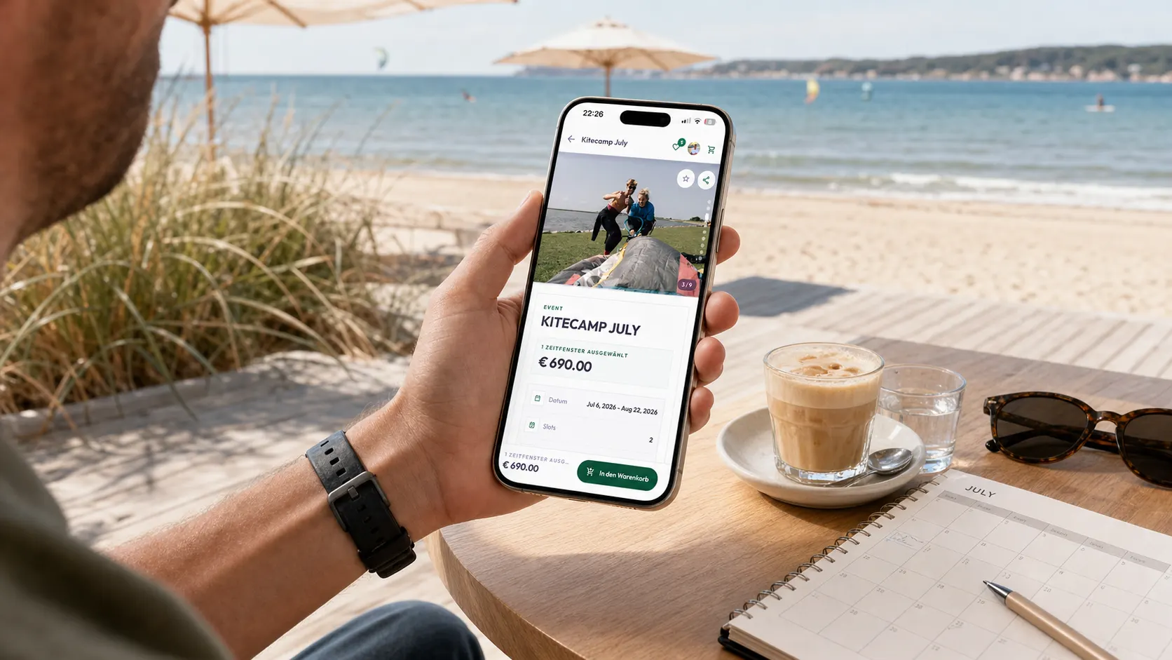 Gast sieht sich ein Kitecamp auf dem Smartphone an einem Tisch am Meer an