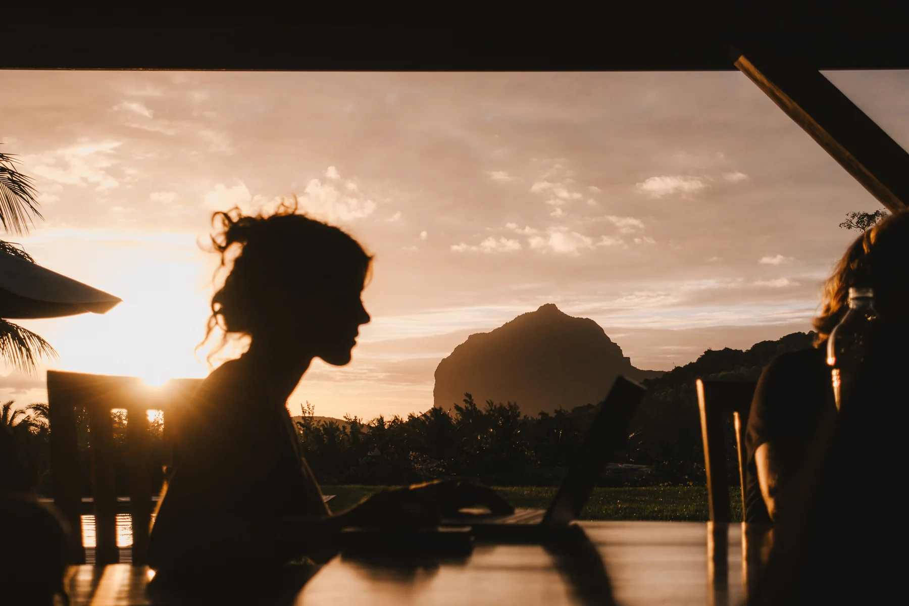 Eine Person arbeitet bei Sonnenuntergang am Laptop, im Hintergrund der Berg Le Morne